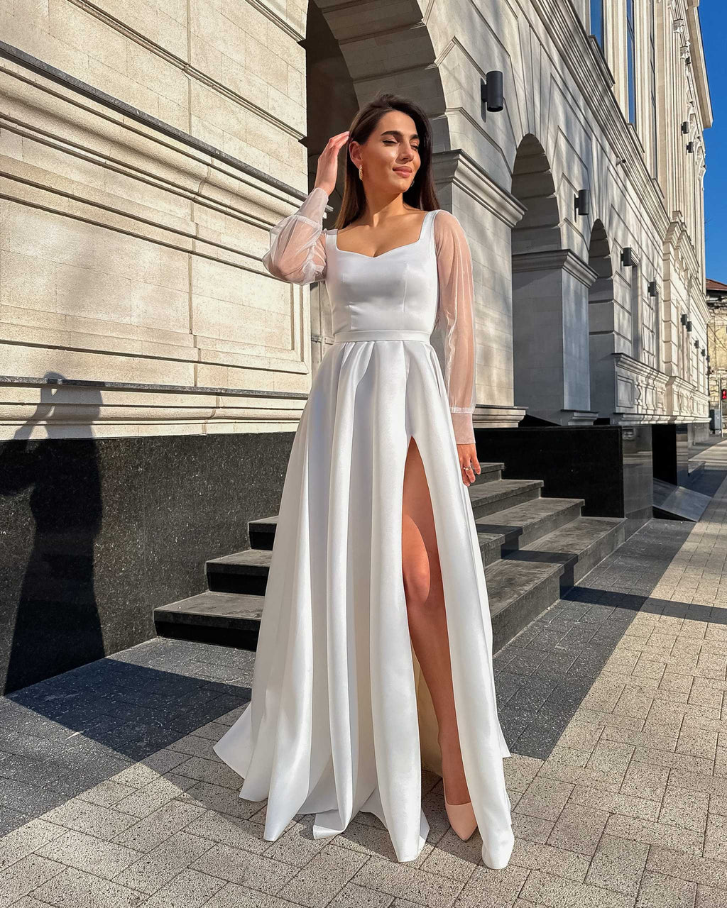 Rochie de mireasa albă lungă din satin elegantă cu șliț și mâneci transparente.
