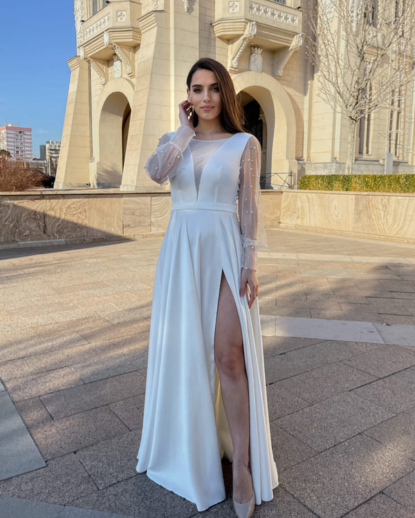 Rochie de mireasa lungă cu mâneci din perle și decolteu în V, fustă cu slit elegant.