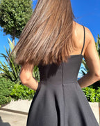 Rochie neagra elegantă scurtă cu bretele și fustă evazată.