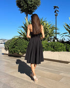 Rochie neagra elegantă scurtă cu bretele și fustă evazată în decor urban.