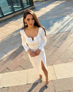 Rochie albă elegantă cu slit și mâneci lungi, potrivită pentru evenimente speciale.